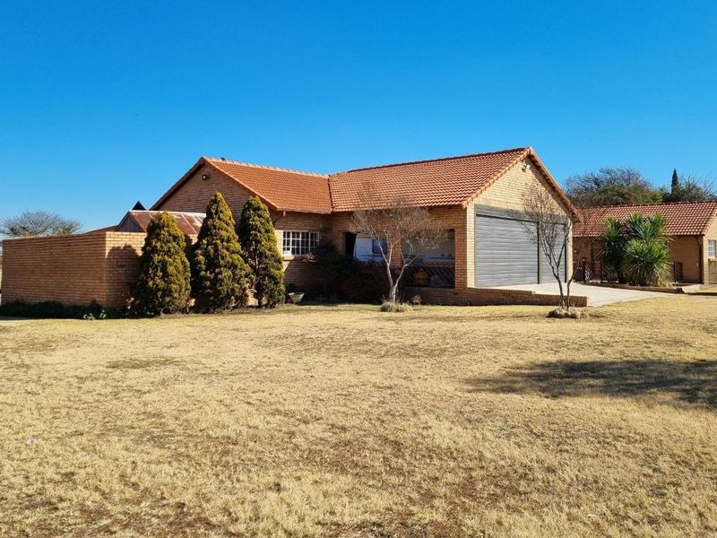 Front view of a face-brick small holding property featuring a tiled roof, integrated garage, and surrounding garden area.