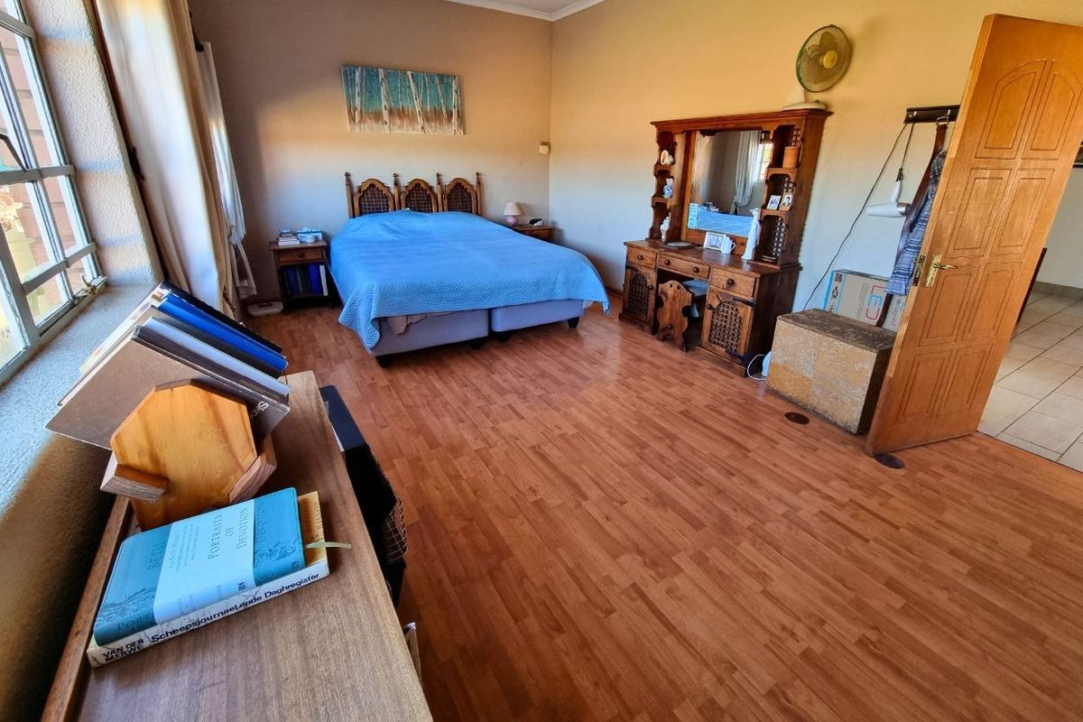 A spacious bedroom featuring laminate flooring, large windows for natural light, and a neutral wall finish, offering a comfortable and functional living space.