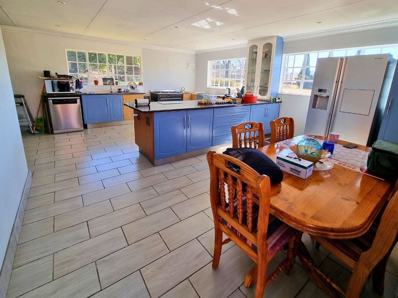 Spacious open-plan kitchen and dining area featuring tiled flooring, blue cabinetry, a central island, and ample natural light from multiple windows.