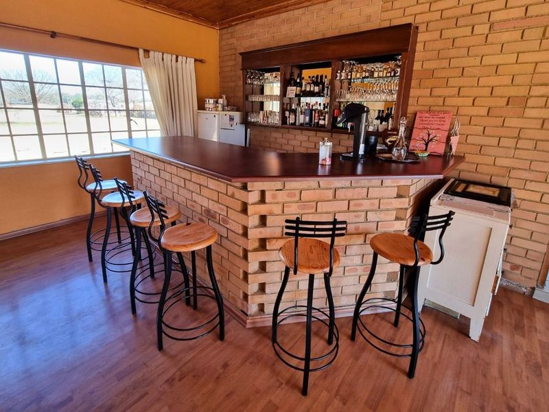 A rustic indoor bar area featuring a built-in brick counter, timber bar top, and integrated mirrored shelving against an exposed brick wall.