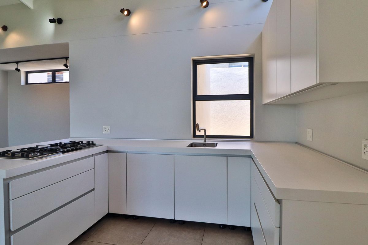 Modern, minimalist kitchen featuring clean white cabinetry, stone countertops, a built-in gas hob, and integrated spotlighting in a bright, open-plan layout.