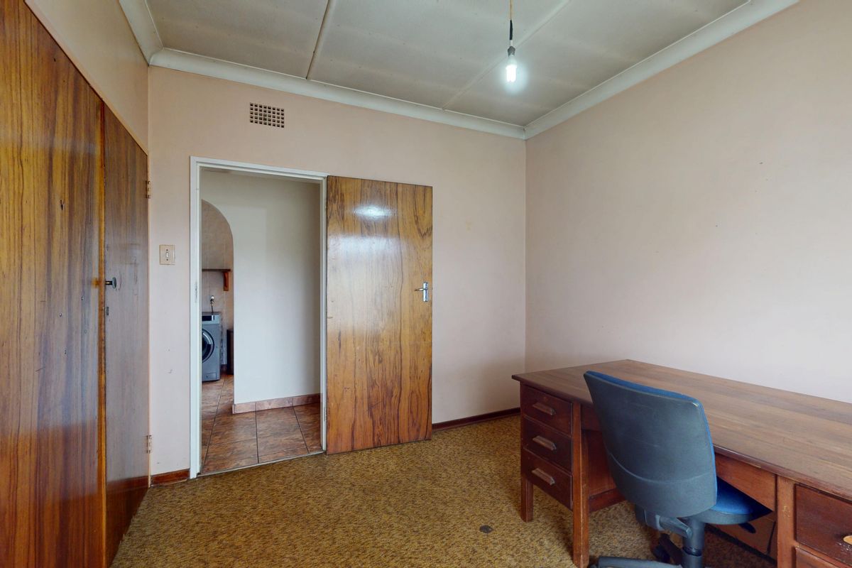 A bedroom featuring built-in wooden cupboards, carpeted flooring, and a coved ceiling, with an adjacent view into a utility area.
