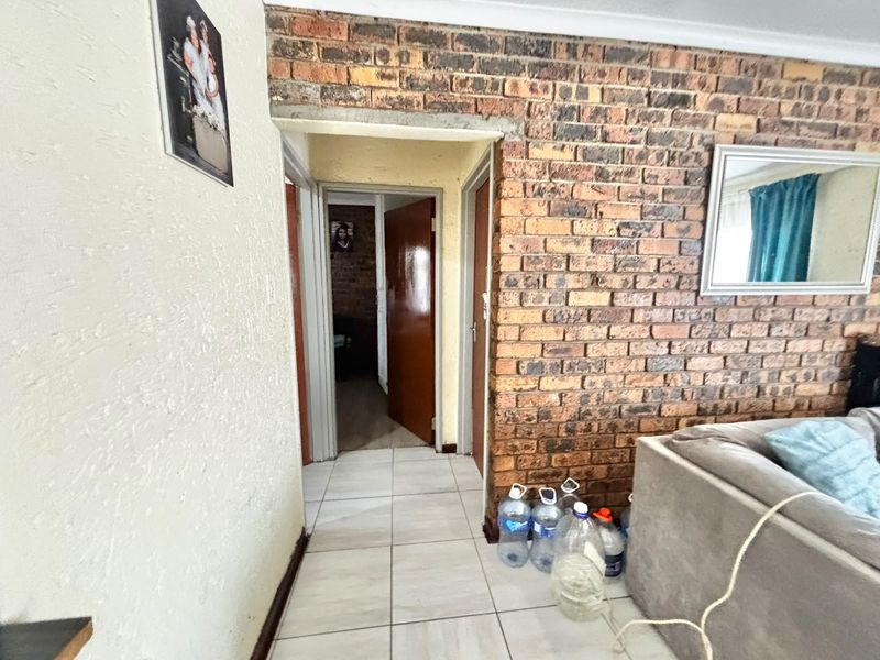 A hallway featuring exposed brickwork and tiled flooring, providing access to adjacent rooms through internal wooden doors.