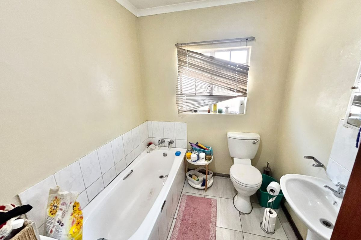 A functional bathroom featuring a bathtub with tiled splashback, pedestal basin, and toilet, with neutral wall finishes and tiled flooring.
