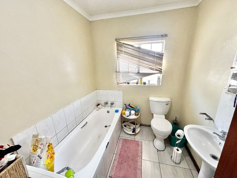 A functional bathroom featuring a bathtub with tiled splashback, pedestal basin, and toilet, with neutral wall finishes and tiled flooring.