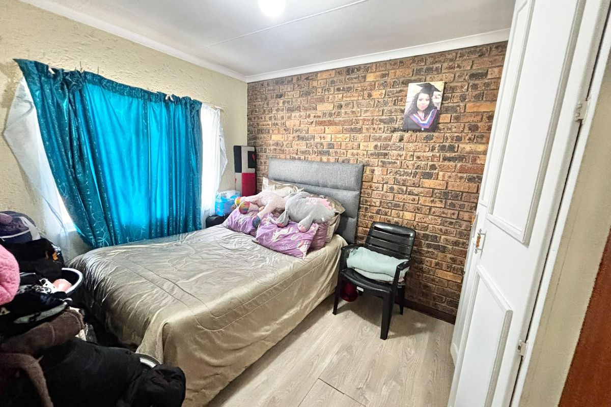 A bedroom featuring an exposed brick accent wall, light-toned laminate flooring, and a built-in cupboard for storage.
