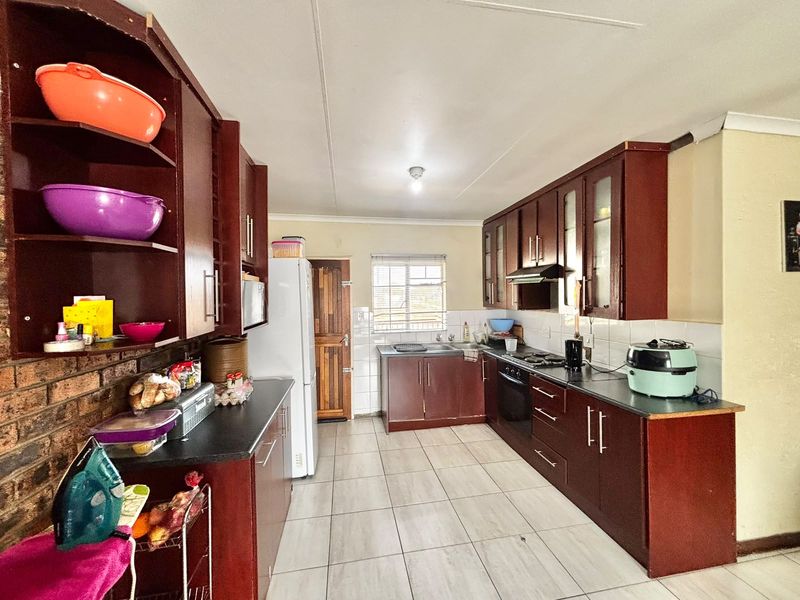 A functional kitchen featuring dark wood cabinetry, laminate countertops, built-in oven, hob, extractor fan, and tiled flooring with a practical layout.