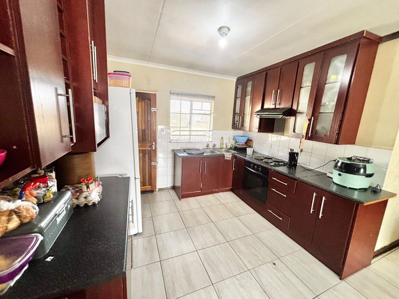 A functional kitchen featuring dark wood cabinetry, laminate countertops, built-in oven, hob, extractor fan, and tiled flooring with a tiled backsplash.