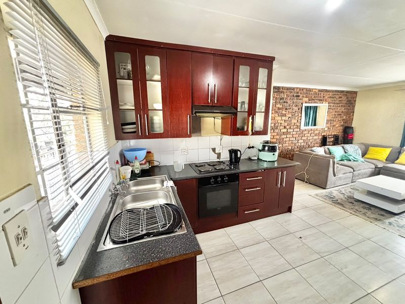 Open-plan kitchen and living area featuring dark wood cabinetry, built-in appliances, tiled flooring, and a rustic exposed brick feature wall.