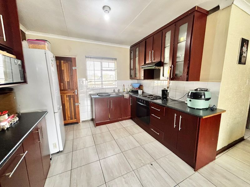Functional kitchen featuring dark wood cabinetry, laminate countertops, built-in oven, hob, extractor fan, and tiled flooring with a neutral backsplash.