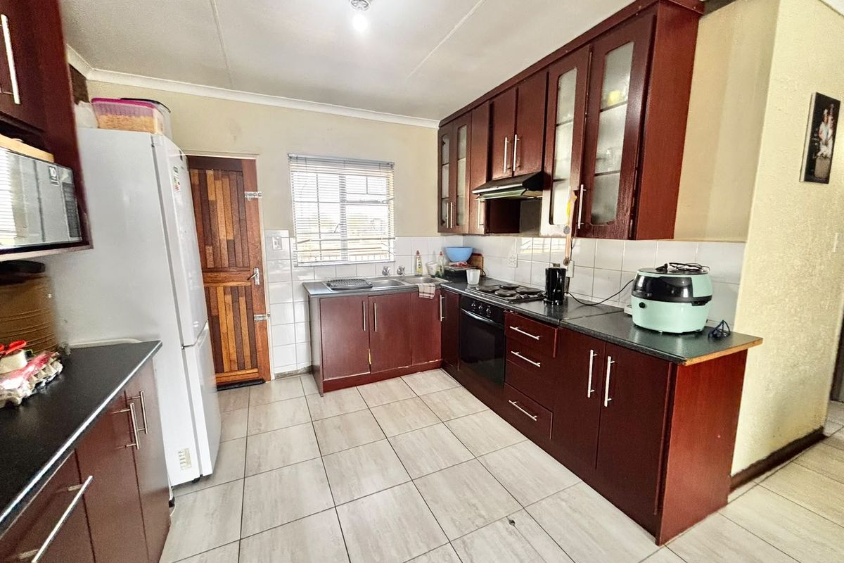 Functional kitchen featuring dark wood cabinetry, laminate countertops, built-in oven, hob, extractor fan, and tiled flooring with a neutral backsplash.