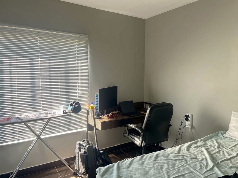 A bedroom featuring tiled flooring, neutral wall paint, and venetian blinds, currently utilized as a functional home office space.