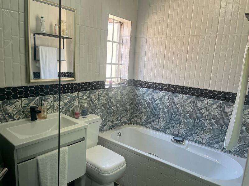 A modern bathroom featuring a vanity with basin, toilet, and bathtub, accented with decorative patterned wall tiles and a black hexagonal border.