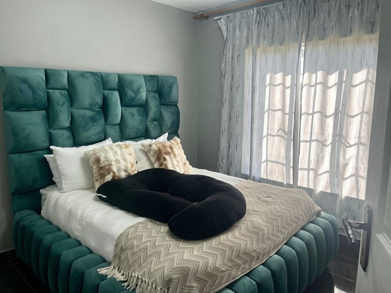 A well-lit bedroom featuring a large upholstered headboard, tiled flooring, and floor-to-ceiling curtains covering the window.