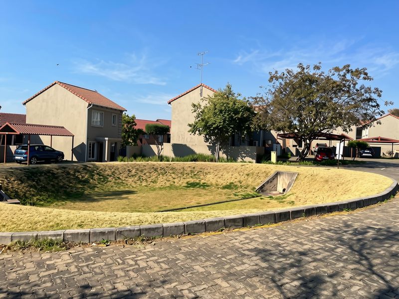 Exterior view of a residential complex featuring paved driveways, carports, and a central drainage basin area with landscaped surroundings.