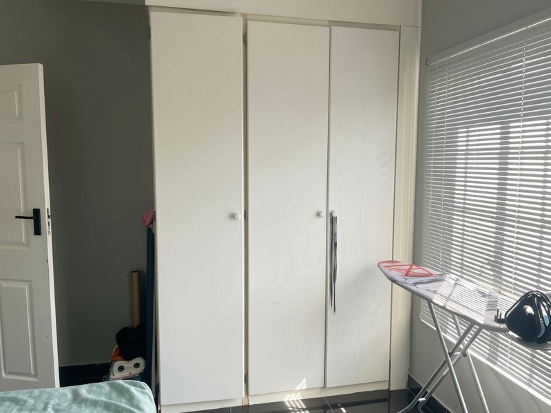 A bedroom featuring a white built-in wardrobe with three doors and venetian blinds on the window.