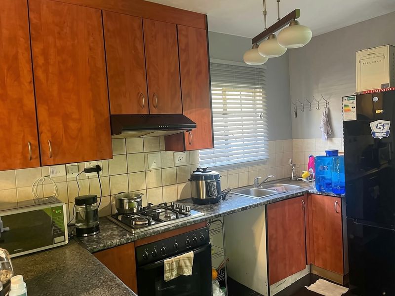 A functional kitchen featuring wooden cabinetry, laminate countertops, a gas hob with extractor fan, and a tiled backsplash.