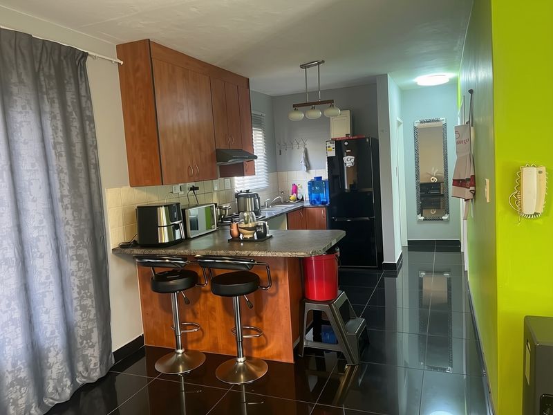 A functional kitchen featuring wood-tone cabinetry, a breakfast bar, tiled backsplash, and dark floor tiles, providing a practical layout for daily use.