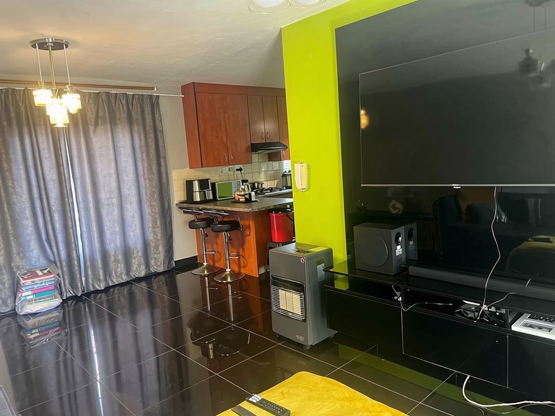 Open plan living area featuring a kitchen with wood-finish cabinetry, breakfast counter, and high-gloss floor tiles, complemented by a vibrant accent wall.