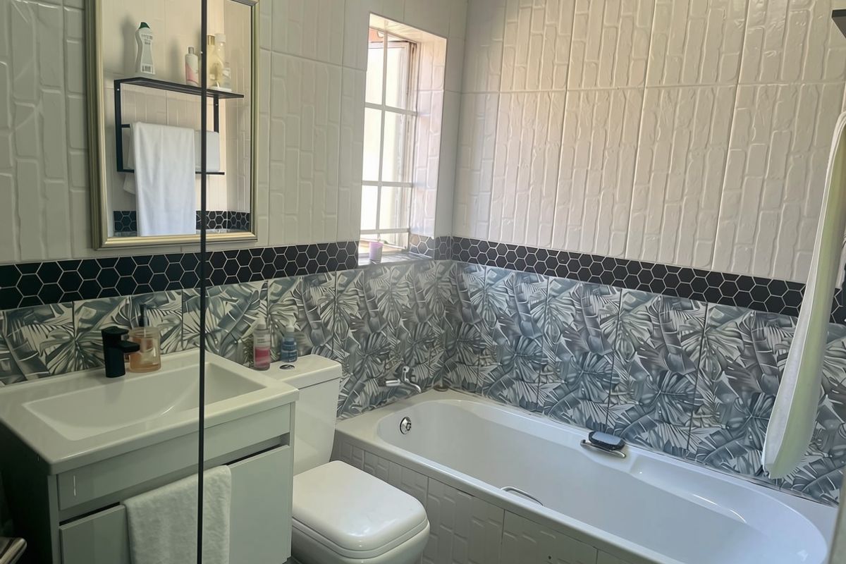A modern bathroom featuring a vanity with basin, toilet, and bathtub, accented with decorative patterned wall tiles and a black hexagonal border.