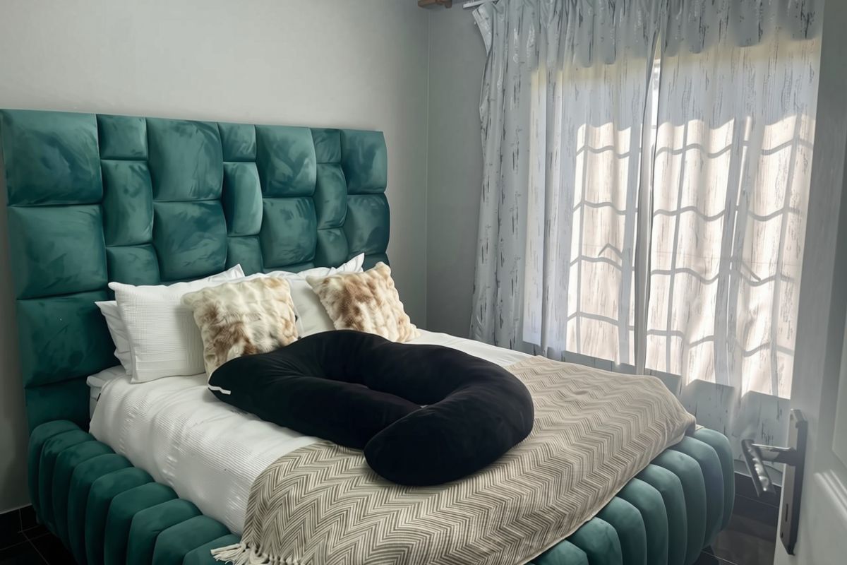 A well-lit bedroom featuring a large upholstered headboard, tiled flooring, and floor-to-ceiling curtains covering the window.