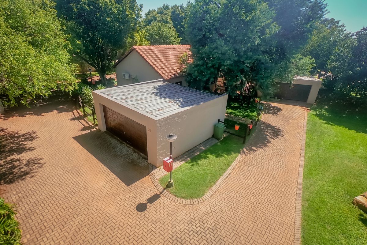 Aerial view of the townhouse property featuring a paved driveway, single garage with a tiled roof, and surrounding landscaped garden area.