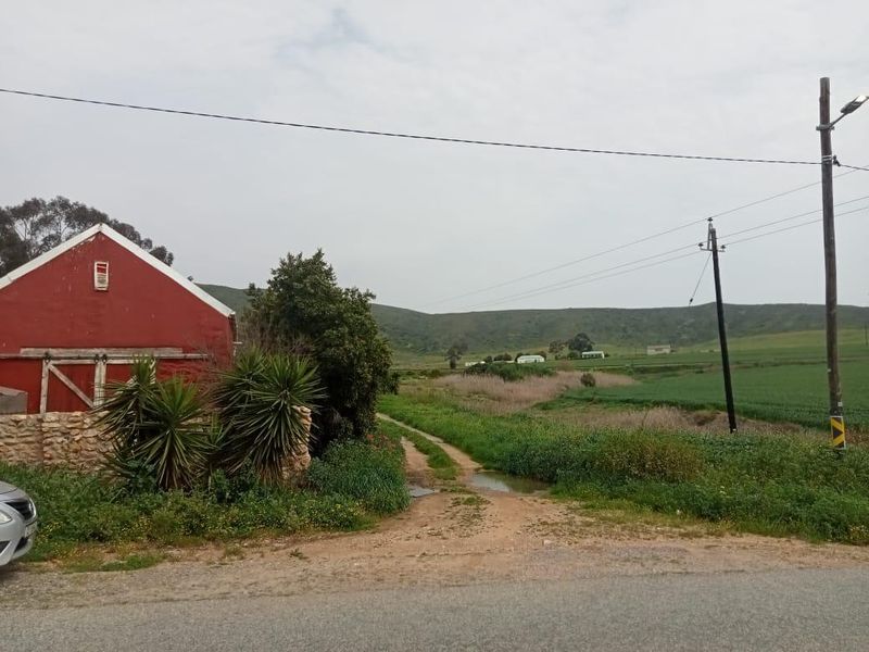 A rural residential land plot featuring an existing red structure, natural landscape, and scenic mountain views from the roadside access point.