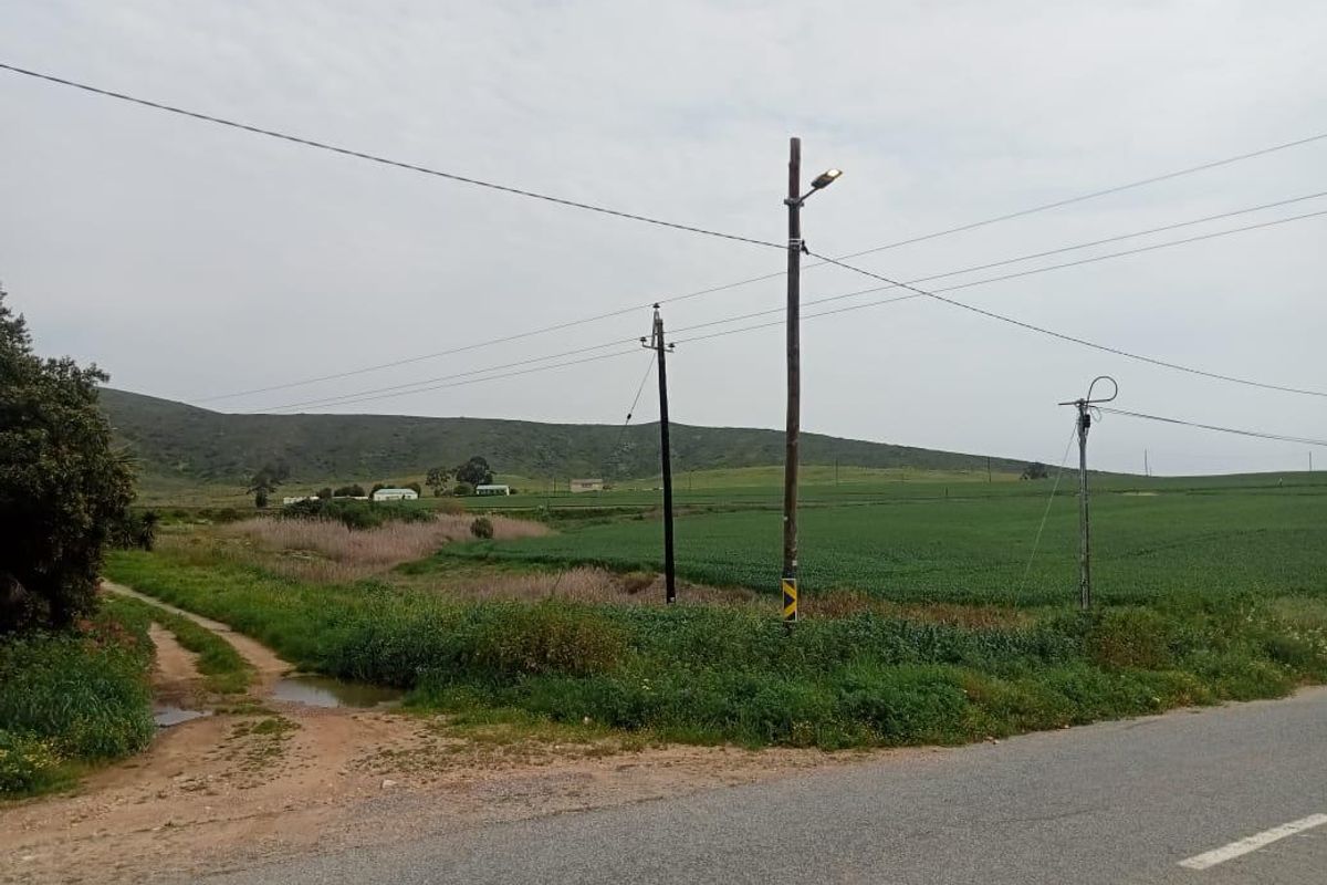 A view of the vacant residential land from the adjacent road, featuring open green fields, natural vegetation, and existing utility poles.