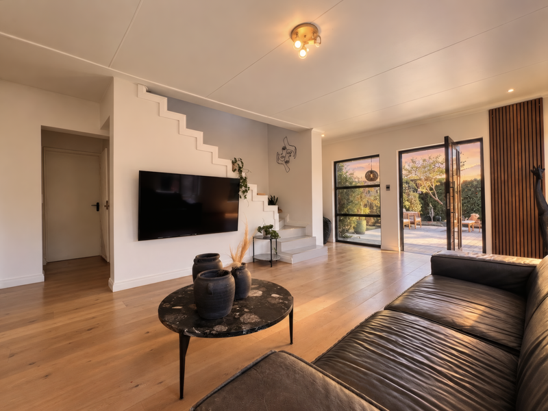 Modern living room featuring light hardwood flooring, a feature staircase, timber slat wall accents, and large glass doors opening to a patio area.