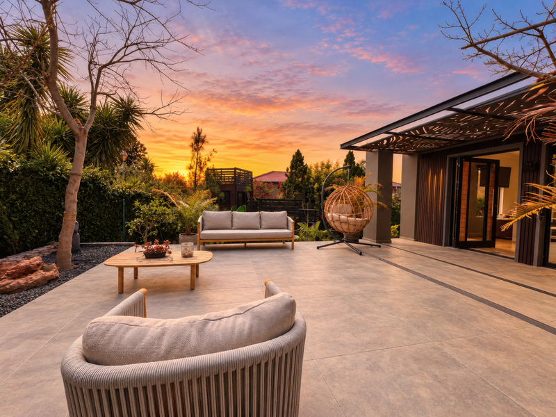 A beautifully maintained outdoor patio area featuring large format tiles, a decorative metal pergola, and seamless access to the interior through bi-fold doors.