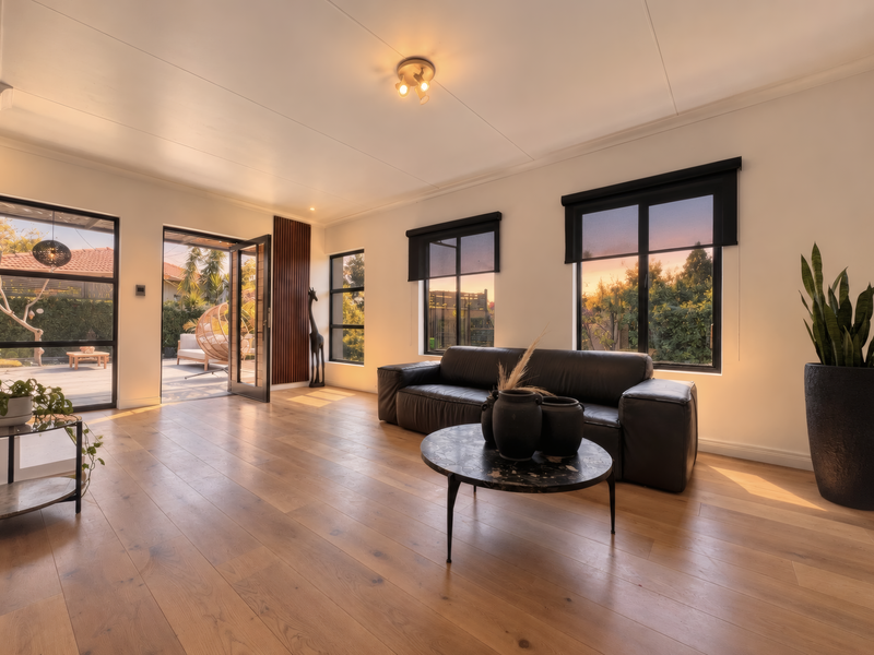 Bright and modern living room featuring warm timber flooring, large black-framed windows, and direct access to an outdoor patio area.