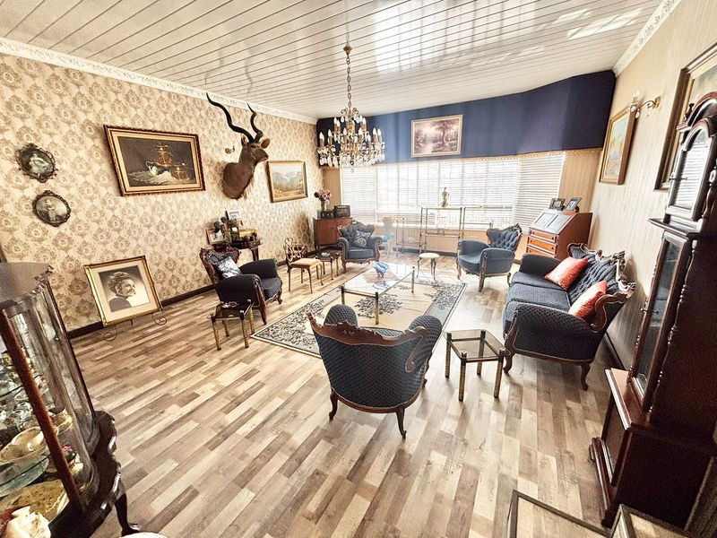 A spacious living room featuring laminate flooring, a decorative chandelier, and coved ceilings, offering a traditional aesthetic with large windows for natural light.