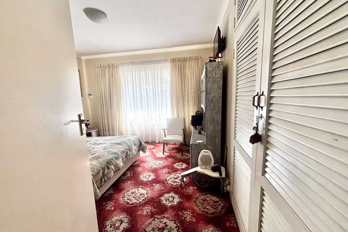 A bedroom featuring built-in louvered cupboards and patterned carpet flooring, offering a functional space with potential for modernization.