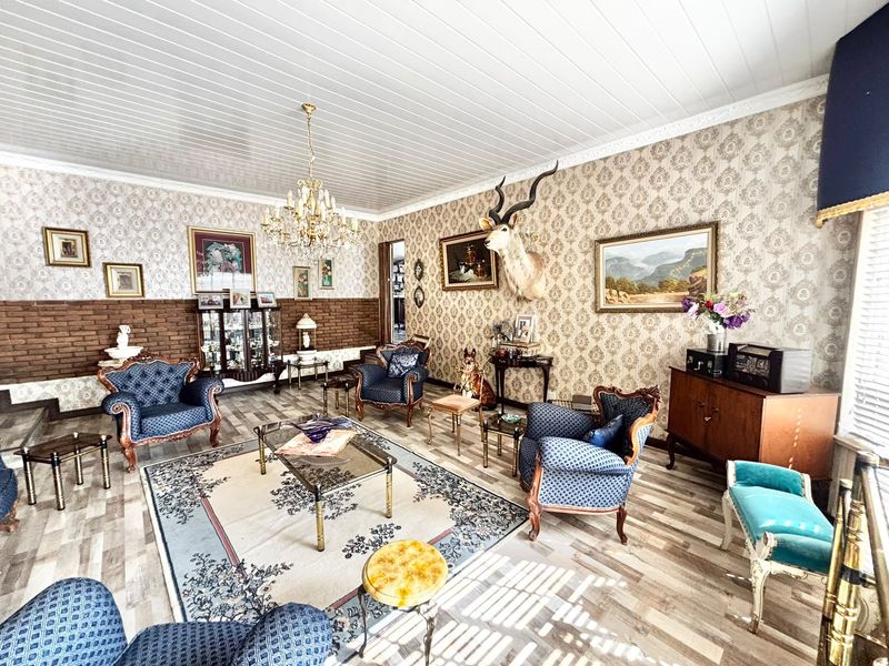 Spacious living room featuring a combination of exposed brick and patterned wallpaper, finished with laminate flooring and a classic tongue and groove ceiling.