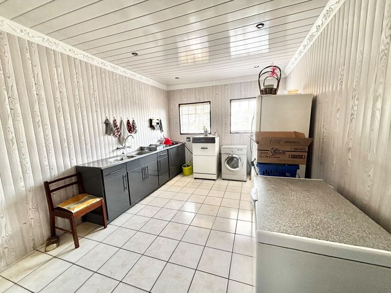 Functional laundry room featuring tiled flooring, built-in cabinetry with a stainless steel sink, and timber-look wall paneling.