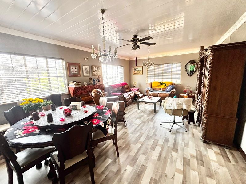 Spacious open-plan living and dining area featuring modern laminate flooring, a ceiling fan, and decorative chandeliers with ample natural light from large windows.