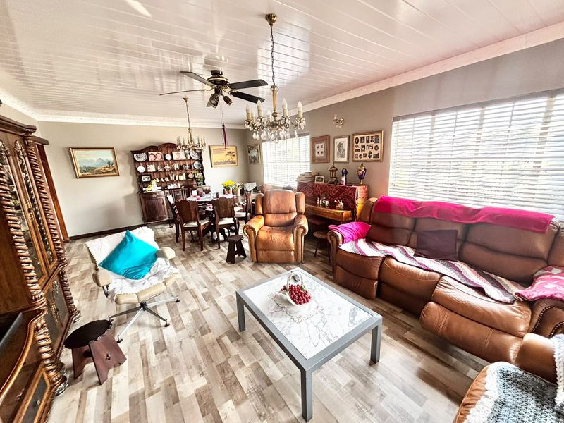 Spacious open-plan living and dining area featuring laminate flooring, coved cornicing, and dual lighting fixtures including a ceiling fan and chandelier.