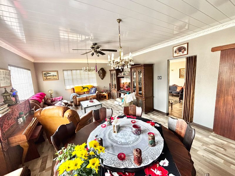 Open plan living and dining area featuring laminate flooring, a ceiling fan, and a chandelier, with a sliding door leading to an adjacent room.