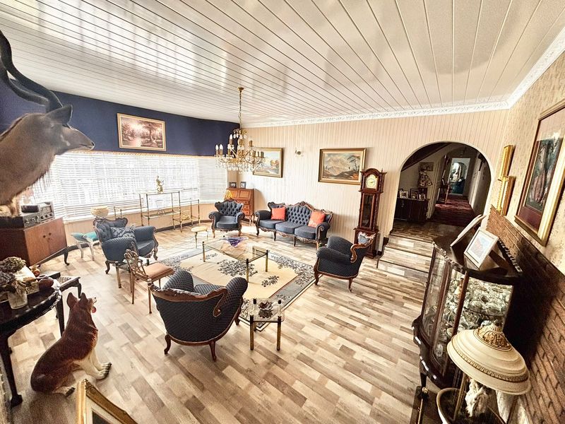 Spacious living room featuring timber-look flooring, a tongue and groove ceiling, and a classic arched entryway leading to the hallway.