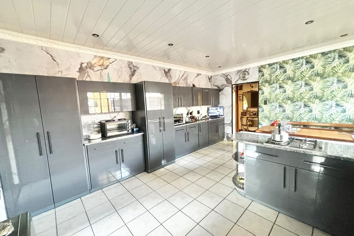 Modern kitchen featuring glossy grey cabinetry, granite countertops, a built-in gas hob, and tiled flooring, accented by decorative wallpaper and a tongue and groove ceiling.