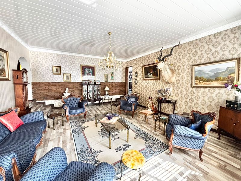 Spacious living room featuring patterned wallpaper, exposed brick accents, wood-look flooring, and a classic chandelier, offering a traditional aesthetic.