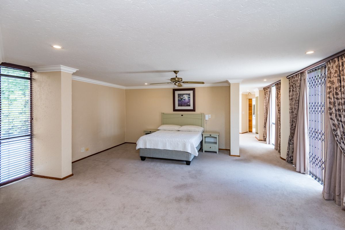 Spacious bedroom featuring neutral carpeting, recessed lighting, a ceiling fan, and large windows with security gates and blinds.