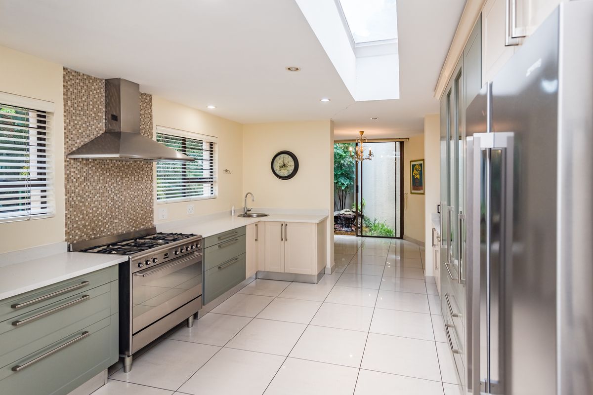 Modern kitchen featuring a gas stove, stainless steel extractor, mosaic backsplash, and a skylight, leading to a bright rear courtyard area.
