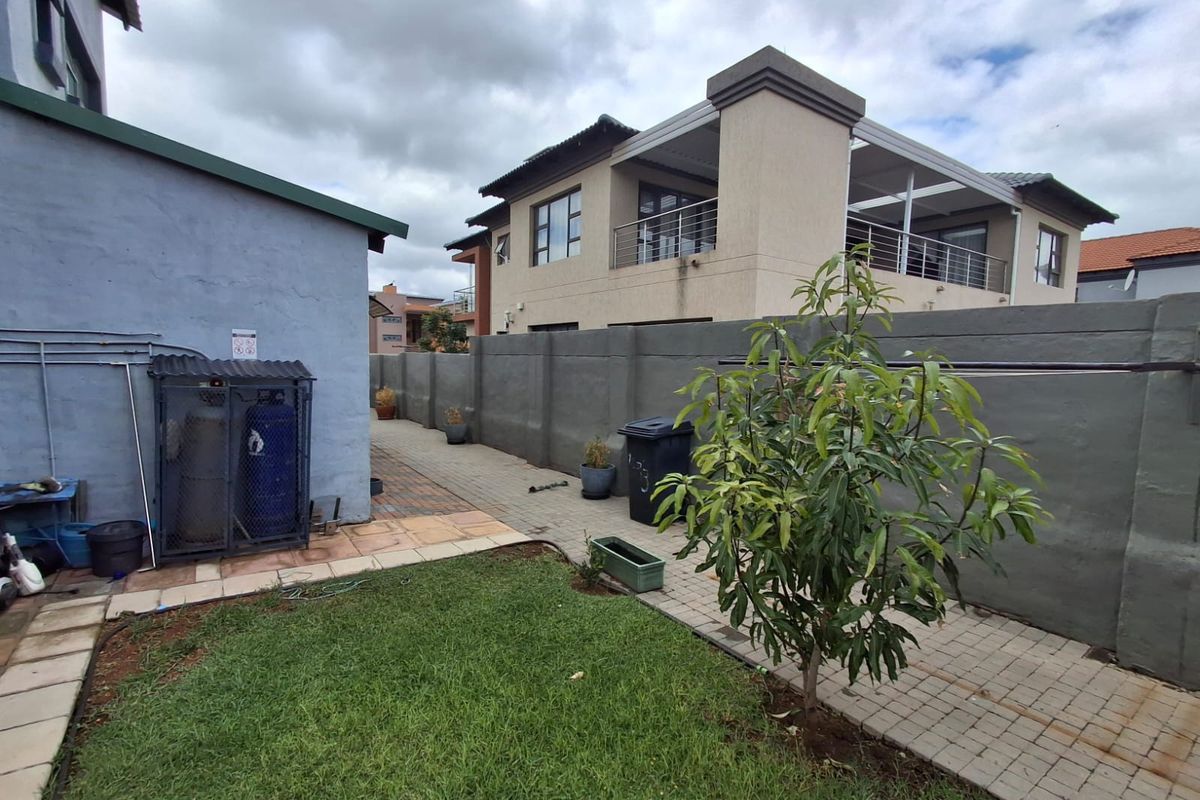 Rear garden area featuring a paved walkway, lawn, and boundary wall, with an external gas cylinder storage unit attached to the side of the house.