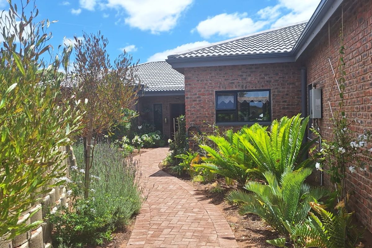 A well-maintained rear exterior view featuring a brick facade, tiled roof, and a paved walkway leading through a landscaped garden.
