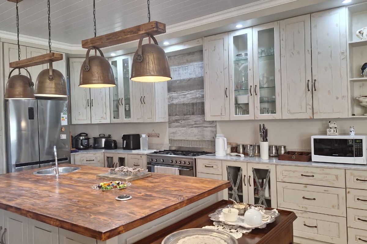 A well-appointed kitchen featuring a large wooden island, custom cabinetry with glass-front details, gas cooking appliances, and a rustic-style ceiling finish.