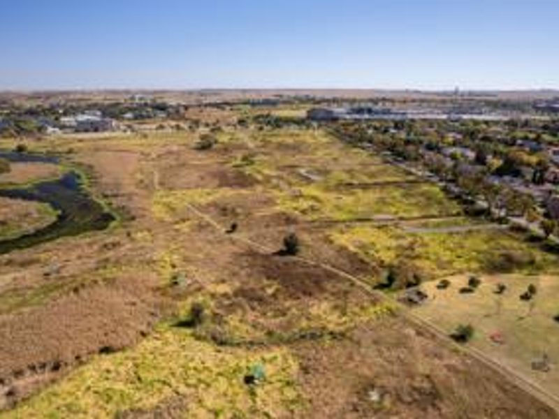 An aerial view of a large, undeveloped residential land parcel situated adjacent to an established suburban neighborhood and natural wetland area.
