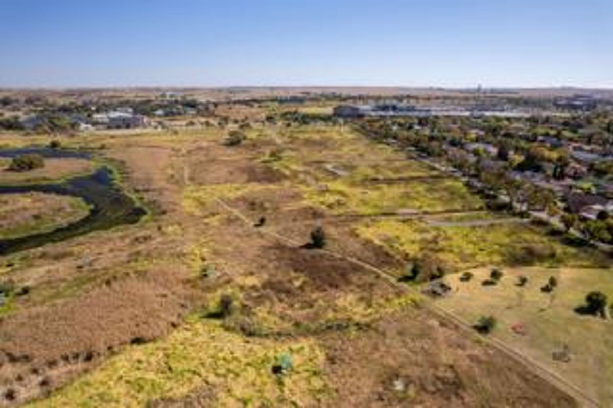 An aerial view of a large, undeveloped residential land parcel situated adjacent to an established suburban neighborhood and natural wetland area.
