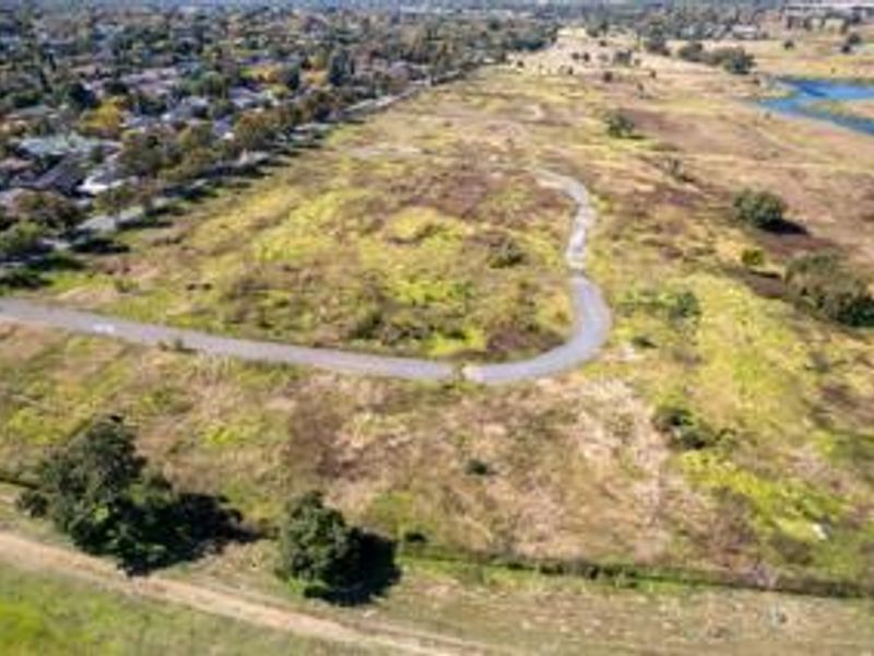 An aerial view of a large, undeveloped residential land parcel featuring a paved pathway and surrounding natural landscape.