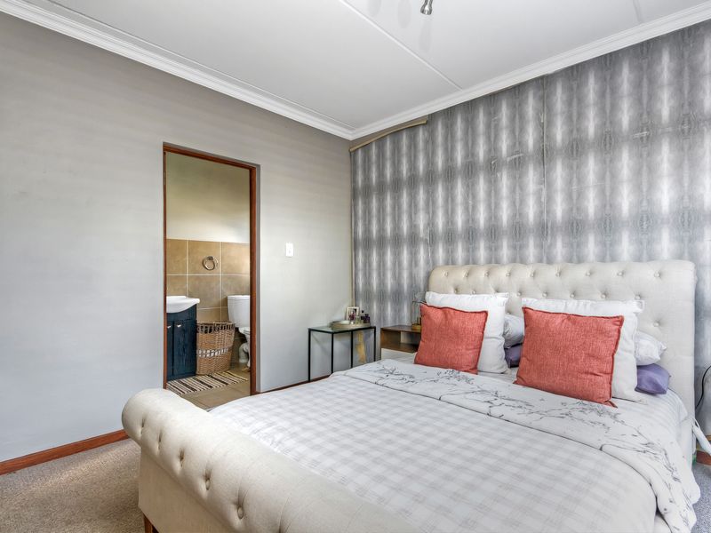 A well-lit bedroom featuring crown molding, carpeted flooring, and direct access to an en-suite bathroom.